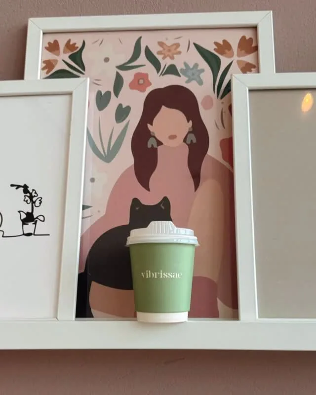 A green Vibrissae coffee cup on a shelf by framed art